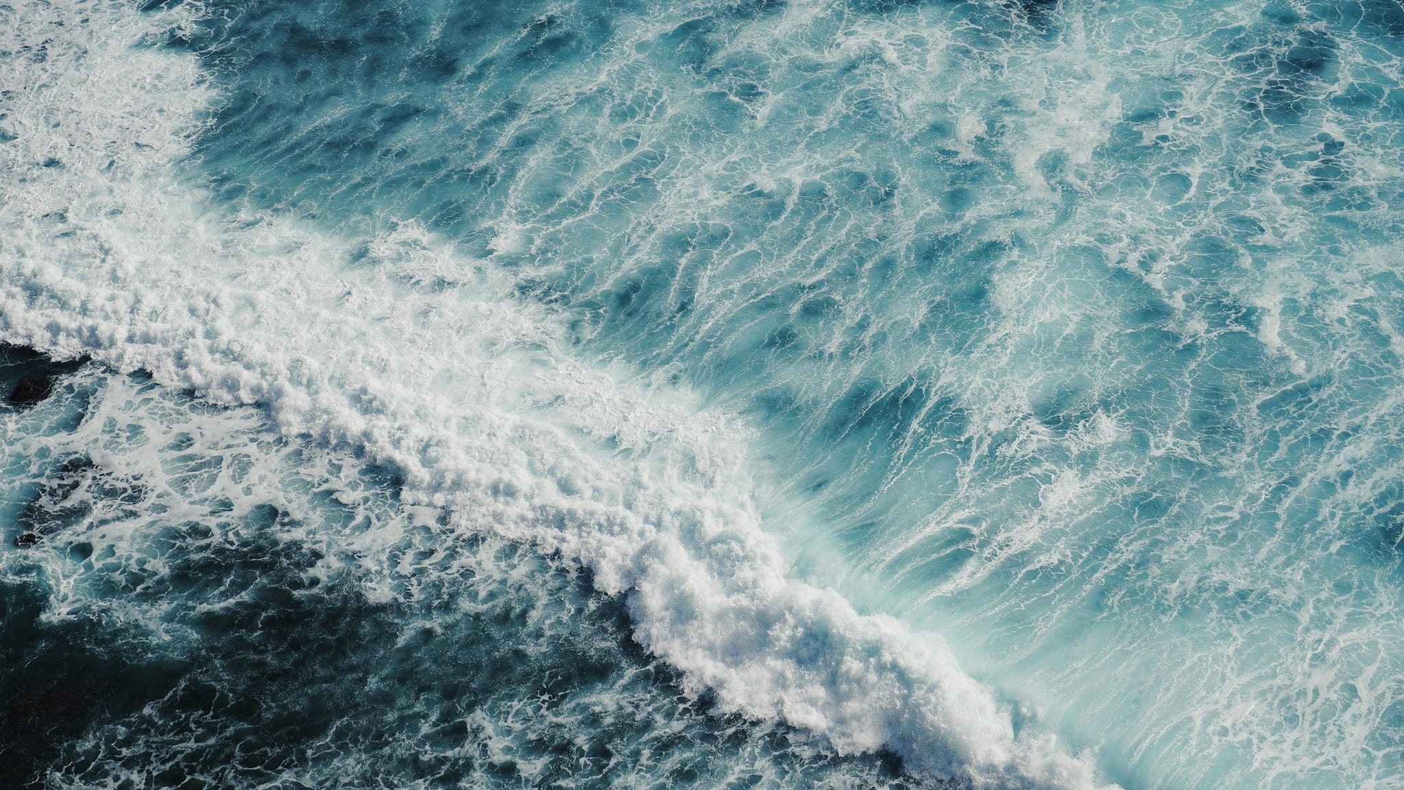 Aerial view looking straight down on a white wave running across deep blue open water