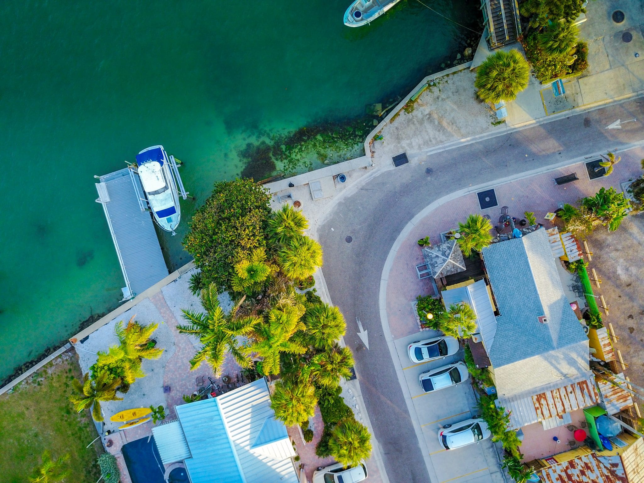Top-down aerial view of boats and a kayak at a palm-lined waterside lane
