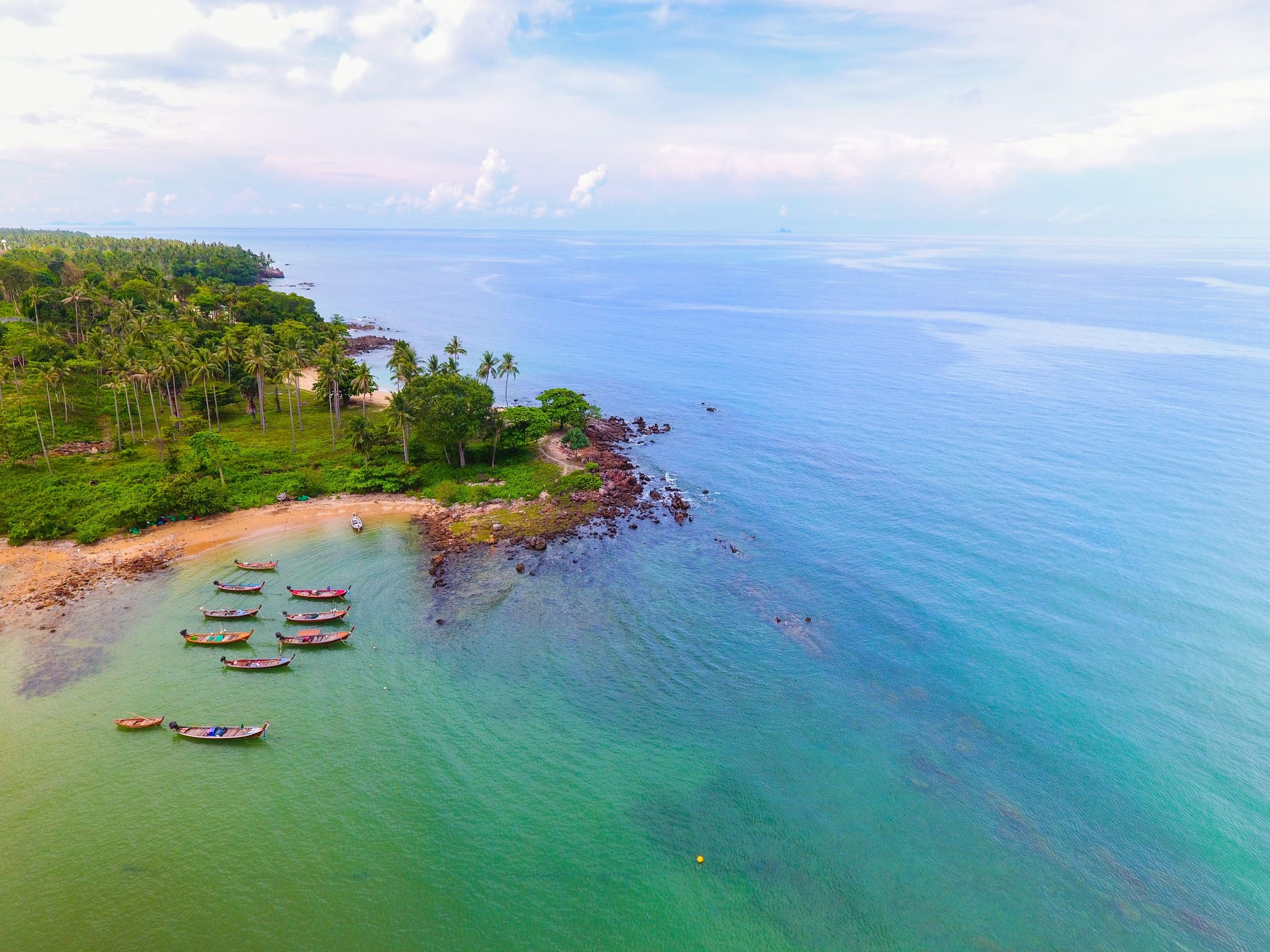 Aerial view of longtail boats resting in a pale turquoise palm-lined cove