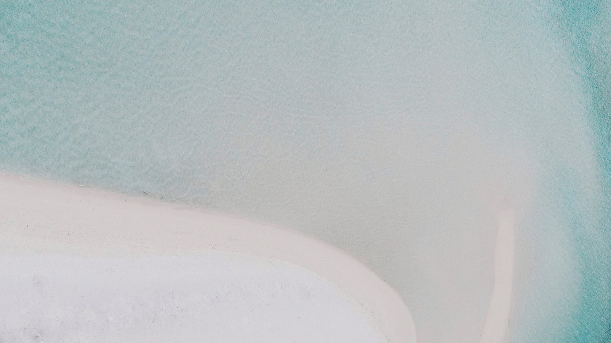 Aerial view looking straight down on a pale sandbar curving into shallow turquoise water